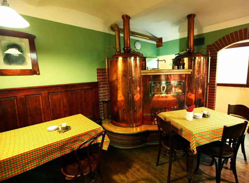 Měděná varna minipivovaru Moritz se znakem MORITZ, mezi stoly restaurace