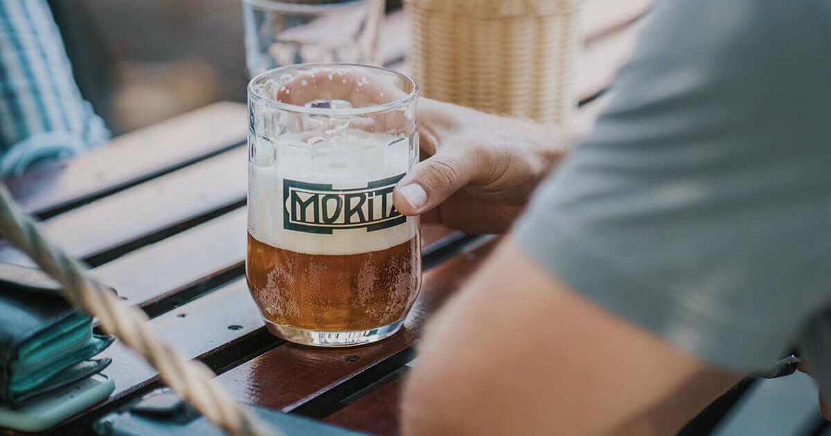 Ruka se sklenicí piva Moritz na zahrádce